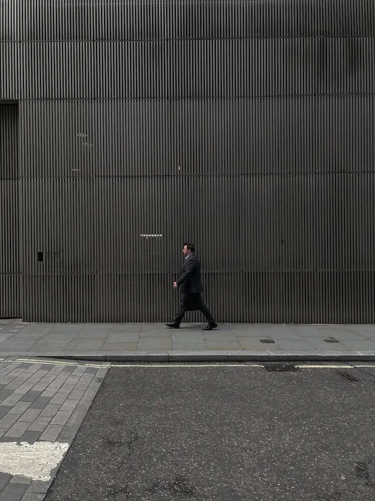 A person in a coat walking past a long ribbed metal wall.
