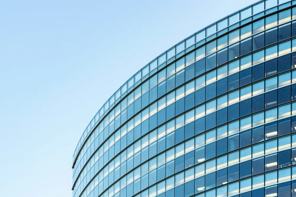 The curved glass front of an office building against a clear sky.