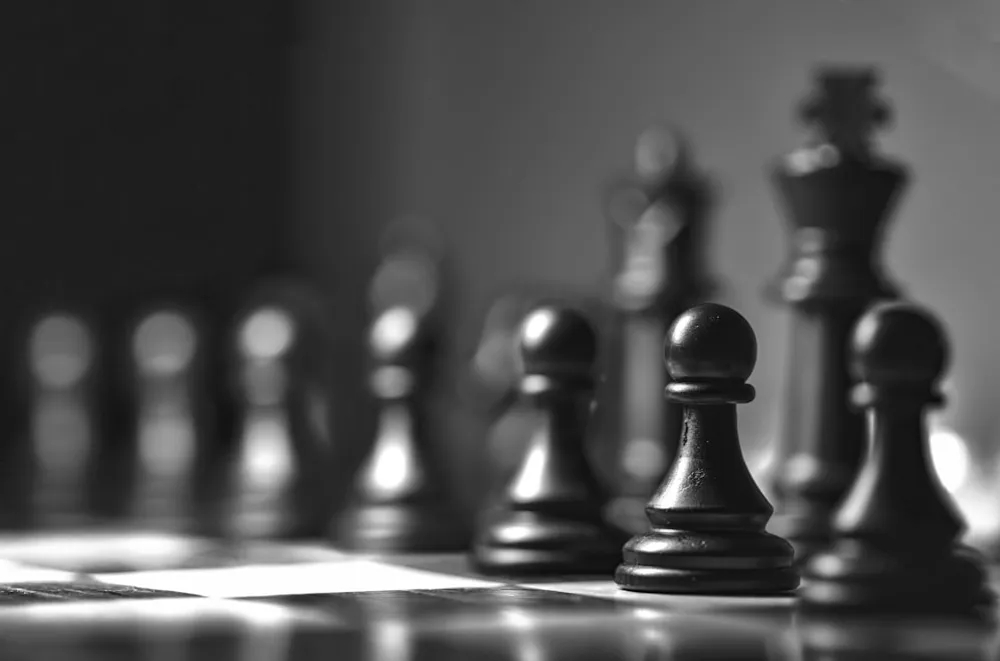 Chess pieces set out on a board, lit from one side.
