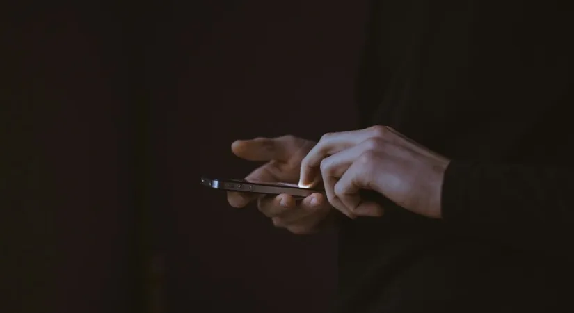 A pair of hands holding a phone in low light.
