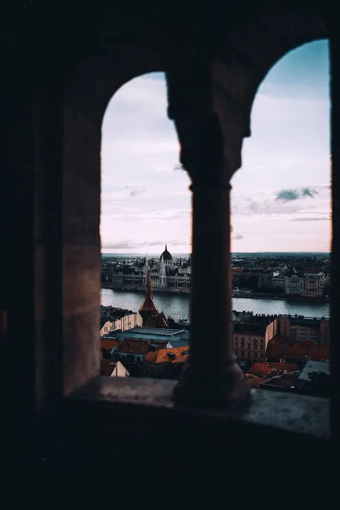 A river city and its parliament building, framed by stone columns.