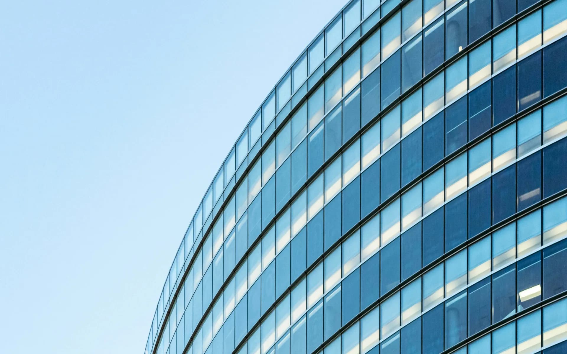 The curved glass facade of an office tower against a clear sky.