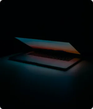 A laptop stands half open on a table in darkness.
