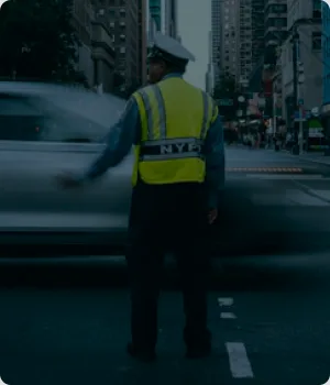 A traffic officer stands on a street beside a moving car.